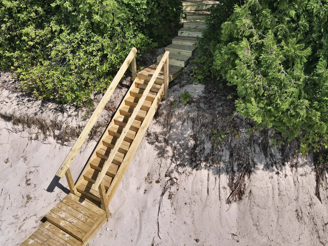 Wooden stairway with handrails leading from the wooded bluff down to the sand