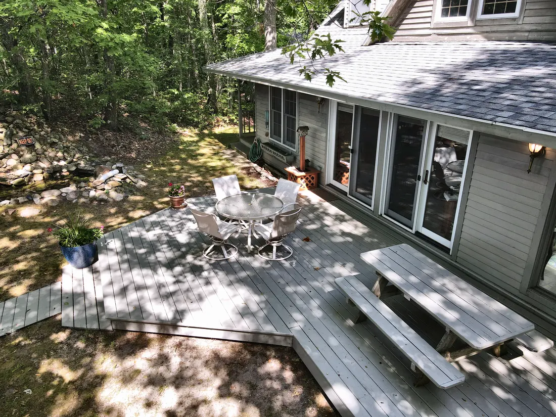 Aerial view of the large painted deck with a round patio table, picnic table and stone garden beside the cottage